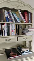 Books arranged on a cream-colored ornate bookshelf, showing multiple titles and stacked books on the desk surface below.