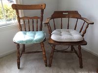 Two wooden chairs, one with arms and one without, each with a seat cushion on carpeted floor near window.