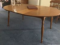 Side view of oval wooden dining table with spindle legs and surface scratches.