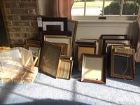 Group of multiple frames leaning against the wall and window, various sizes and styles visible