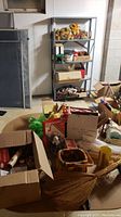 Wide view showing shelves and table full of assorted holiday decorations including wreaths on the top shelf and various boxes and loose decorations below.