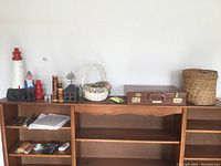 View of all items on wooden shelving unit against white wall, including lighthouse lamp, baskets, figurine, briefcase, waste basket, sponge, and comb.