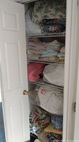 Closet shelves filled with folded linens including sheets, blankets, comforters, and linens in plastic bags at bottom