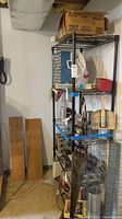 Full view of metal shelving unit loaded with basement items including small plastic drawer organizer and various tools and boxes.