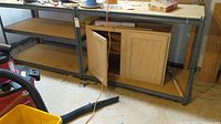 Two matching shelving units with metal frames and particle board shelves positioned side by side in a basement, with a cabinet inside one shelf (cabinet excluded).