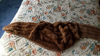 Full view of the mink stole laid out on a floral quilt, showing the length and brown fur texture.