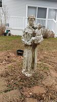 Full view of the outdoor Saint Anthony statue standing in a grassy area showing overall size and weathering.