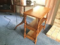 Round pedestal table with a round top and three feet, medium brown finish, visible wear and scratches, shown with other table in background.