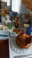 View of all items including chicken-shaped bowl, vases, decanters, plates, and blue Pyrex dish on table.