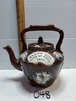 Full view of antique Measham teapot with handle and spout, showing overall shape and size relative to ruler in background.