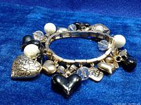Silver-tone expandable charm bracelet featuring various charms such as solid black and silver hearts, silver hearts with embossed hearts pattern, a bow charm, clear faceted beads, white faux pearls, and a 'BJ' engraved heart charm.