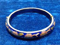 Blue and gold tone cloisonne flower bangle bracelet displayed closed on a blue fabric background.