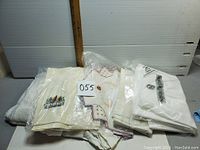 Small lot of assorted vintage linens folded and stacked with white plastic table skirt included visible beneath linens.