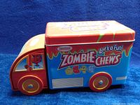 Front-side view of the truck candy tin showing colorful Zombie Chews branding and cartoon characters on the cab window.