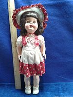 Full view of the Roddy Walker doll standing next to a ruler for size reference, wearing original clothing including dress, bonnet, shoes, and socks.