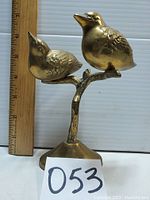 Brass bird figurine showing scale against a wooden ruler approximately 7 inches tall.