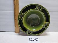 Top view of the green glazed pottery ashtray showing central bowl area, cigarette rests, and compartments, with ruler for size reference.