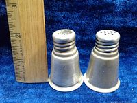 Pair of vintage sterling silver salt and pepper shakers, showing their height against a ruler and placed on a blue velvet background