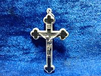 Front view of silver tone crucifix pendant with black inlay and Jesus figure on blue fabric background.
