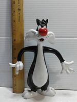 Front view of Sylvester the Cat figure standing next to ruler showing approximate 8-inch height.