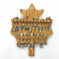Front view of the maple leaf-shaped wooden spoon holder filled with 22 collectible spoons with various enamel crests and silver-toned bowls.