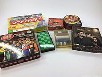 Photo showing six different games and sets including Monopoly Canada edition, Angry Birds puzzle, Coca-Cola NASCAR board game, poker chips, New Moon themed game, and magnetic chess and checkers set.