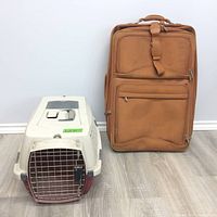 Pet carrier and brown suitcase side by side on floor showing full profile