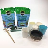 All items including two bags of Miracle-Gro Seed Starting potting soil, multiple ceramic pots and bowls, a blue plastic pot, a wooden dibber tool, and a green handheld sprinkler.
