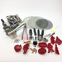 Wide view of entire kitchenware lot showing cutlery, tongs, sieves, splash guards, various cookie cutters, and other utensils arranged on white background.