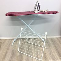 Full view showing ironing board with iron on top and white metal drying rack beneath.