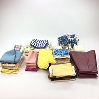Overall view of all linens including oven mitts and folded towels and table cloths.