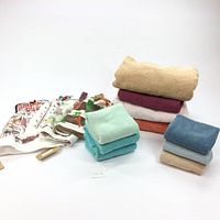 Stack of assorted bath towels in various colors with smaller hand towels folded beside them along with some dish towels