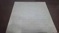 Front cover of Pink Floyd The Wall vinyl album featuring white brick wall design with some wear and surface marks.