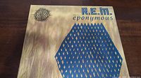 Front cover of R.E.M. Eponymous vinyl album showing the title and artwork with blue hexagonal pattern on a light brown background.