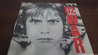 Front cover of the U2 War vinyl album showing a close-up of a child's face, lip pierced, with 'U2 WAR' text in red.