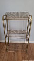 Front view of the vintage metal record holder rack showing all three tiers with wire slots for organizing vinyl records vertically. Gold-tone metal frame with rounded side handles visible.