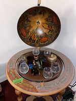 Open antique map-design bar globe showing six glasses and empty liquor bottles on wood stand