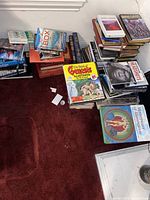 Multiple stacks of mixed hardcover and paperback books on red carpet floor