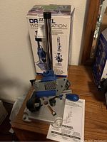 Dremel 220 Work Station tool stand with box and manual displayed on wooden surface, front view.