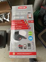 Boxed Genie Ultra-Quiet Smart Garage Door Opener showing branding and features including 1 1/4 HP motor, battery backup, LED lighting, and smart home connectivity.