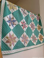Full view of quilt showing patchwork star blocks on teal and white background and white border with diamond quilting stitches.