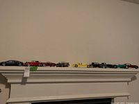 Nine model cars displayed on a white shelf, viewed front-on in a single row