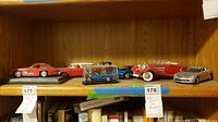 Shelf view showing six die-cast cars on a wooden shelf