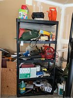 Wide photo of black shelving unit filled with assorted household, gardening, and maintenance items for overview.