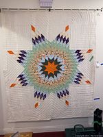 Full view of handmade quilt with multicolor star design and white background hanging on wall.