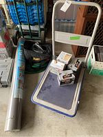 Photo of metal rolling cart loaded with pest control foggers, black Meguiar's car buffer bag, and rolled weed block fabric beside cart.