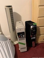Photo of the three appliances lined up: a white Seville Classics tower fan, a white DeLonghi heater, and a black Honeywell heater.