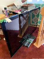 Sony 60-inch LCD TV screen shows bezel and remote control placed beneath TV leaning on a carpet next to a railing.
