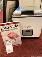 Sous Vide Supreme Demi sous vide machine along with the cookbook 'Sous Vide for the Home Cook' placed next to each other.