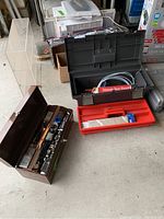 Overview photo showing two open tool boxes with assorted tools inside. Brown box with hand tools and black/red box with plumbing wrench and other tools.